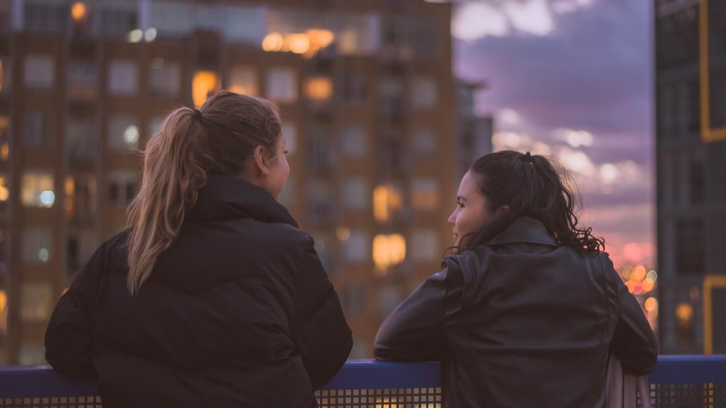 2 women talking in front of buildings